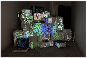 Mixed media installation containing suitcases with multicolored graphics upon them.