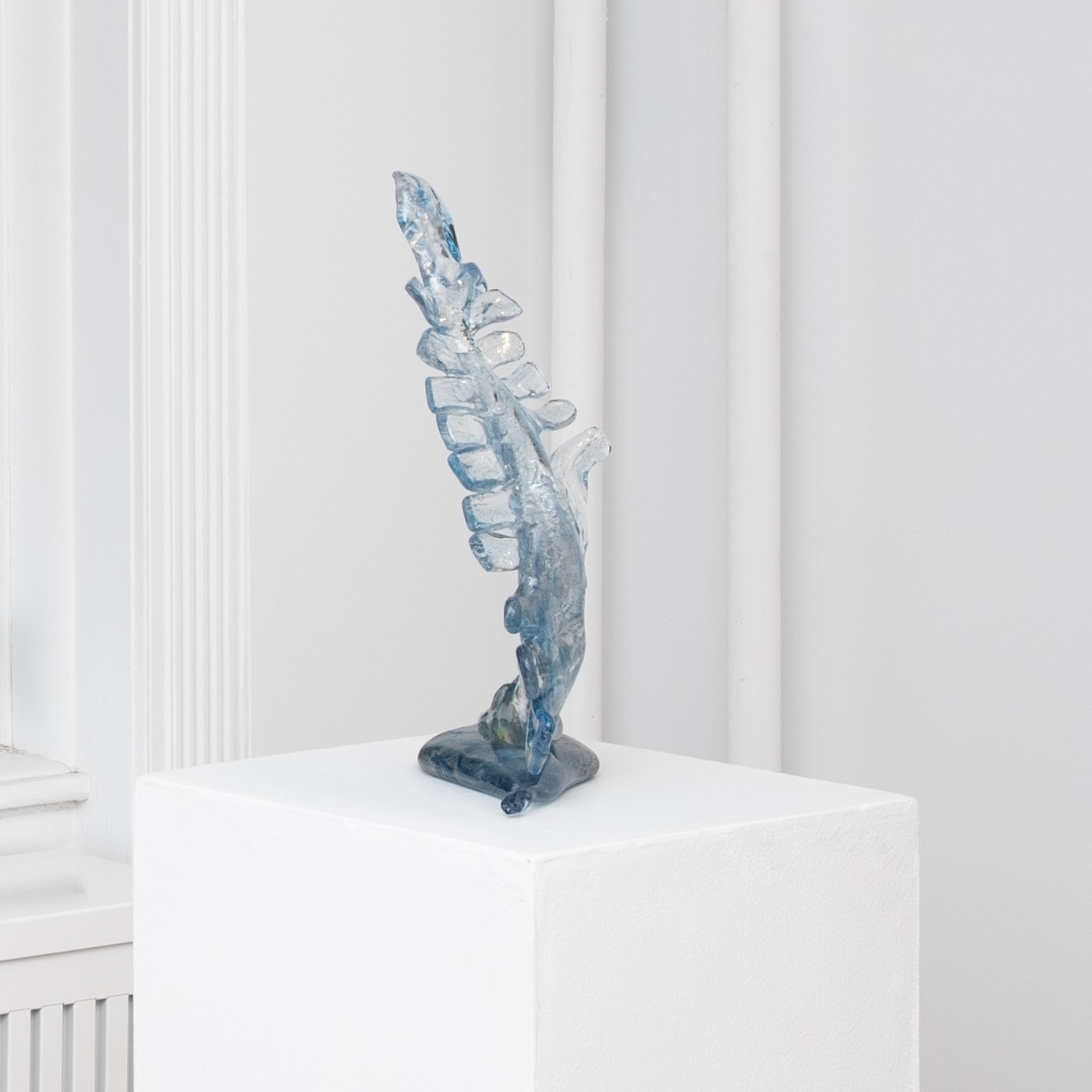Glass abstract sculpture on a white pedestal in a white-wall gallery.