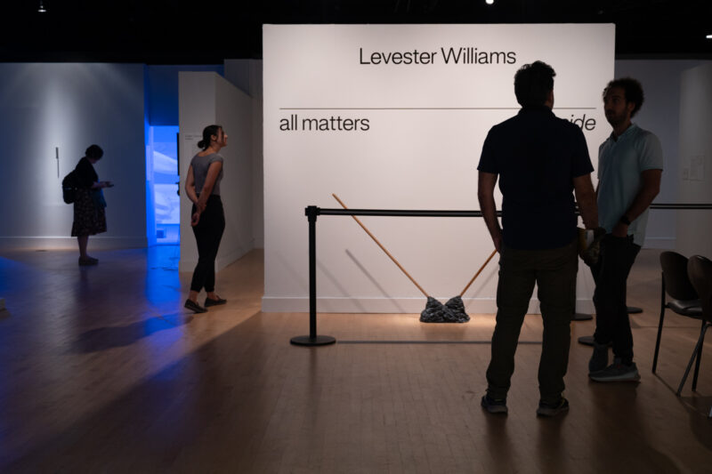 Gallery visitors stand near the entrance to the exhibition "Levester Williams: all matters aside." Wall text announces the name and artist of the exhibition.