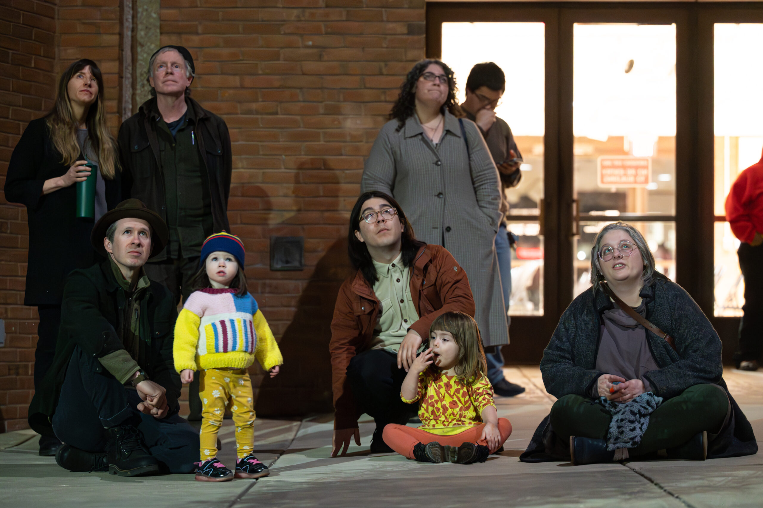 A group of individuals are both seated and standing while looking up at a projection. There are both children and adults in the group