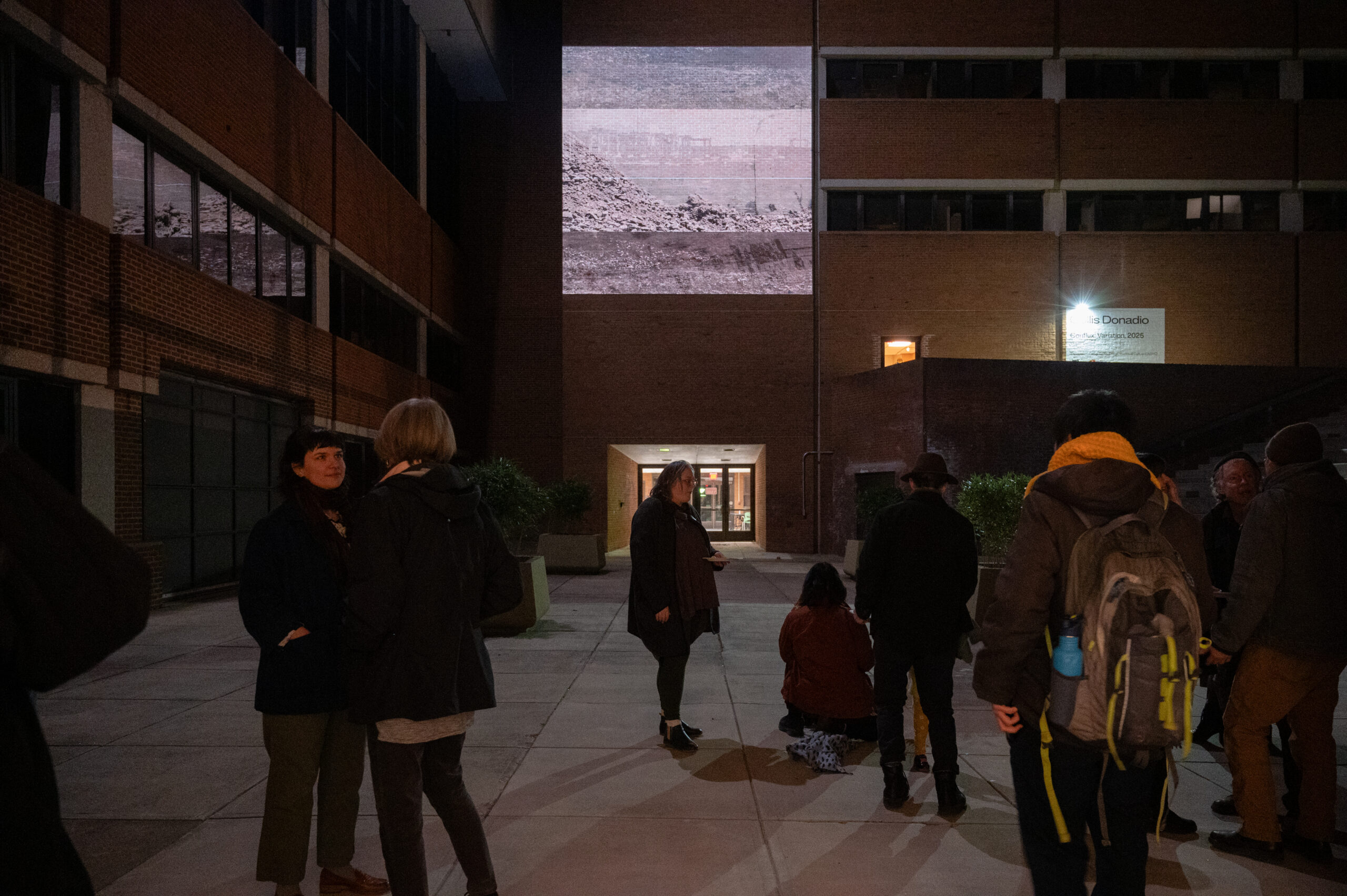 A group looks up at a video projection on the side of a red brick building.