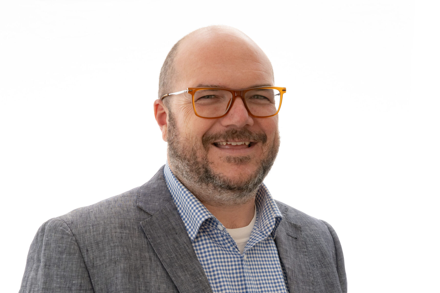 Headshot of a white man with glasses smiling at the camera. He wears a grey blazer and a gingham blue dress shirt.