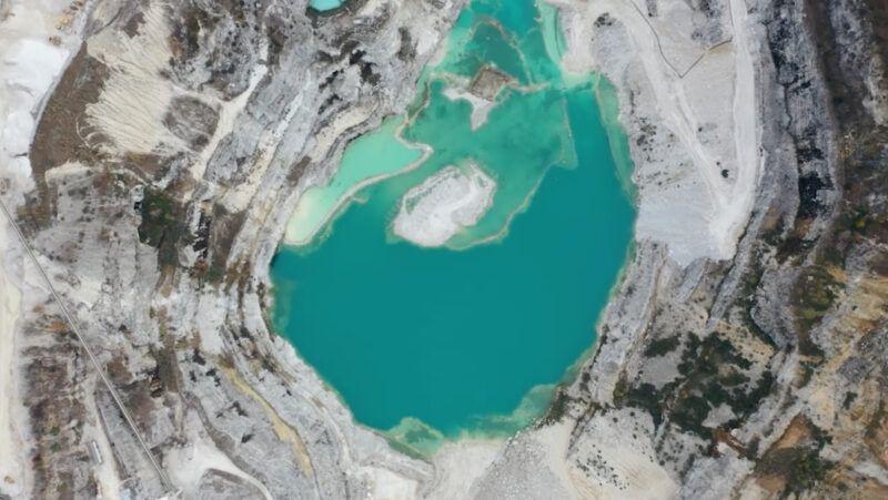 Drone image of a marble quarry. At the center of the image is a bright teal pond, surrounded by white and grey rocks.