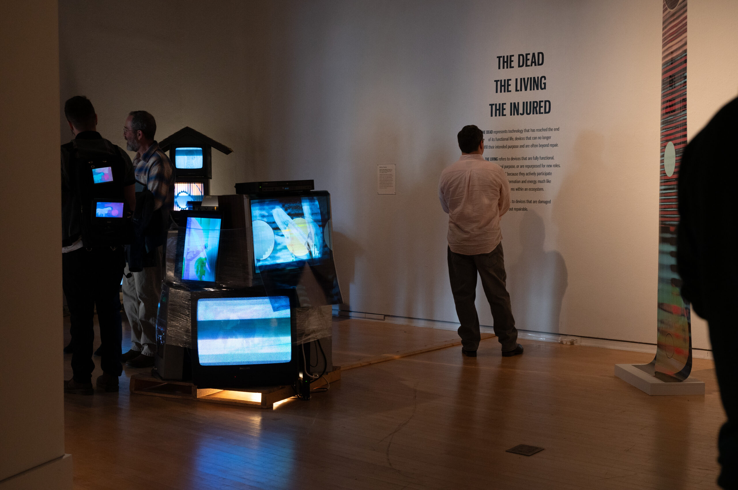 Man standing next to a mixed media sculpture reads didactic text on the wall of the gallery.