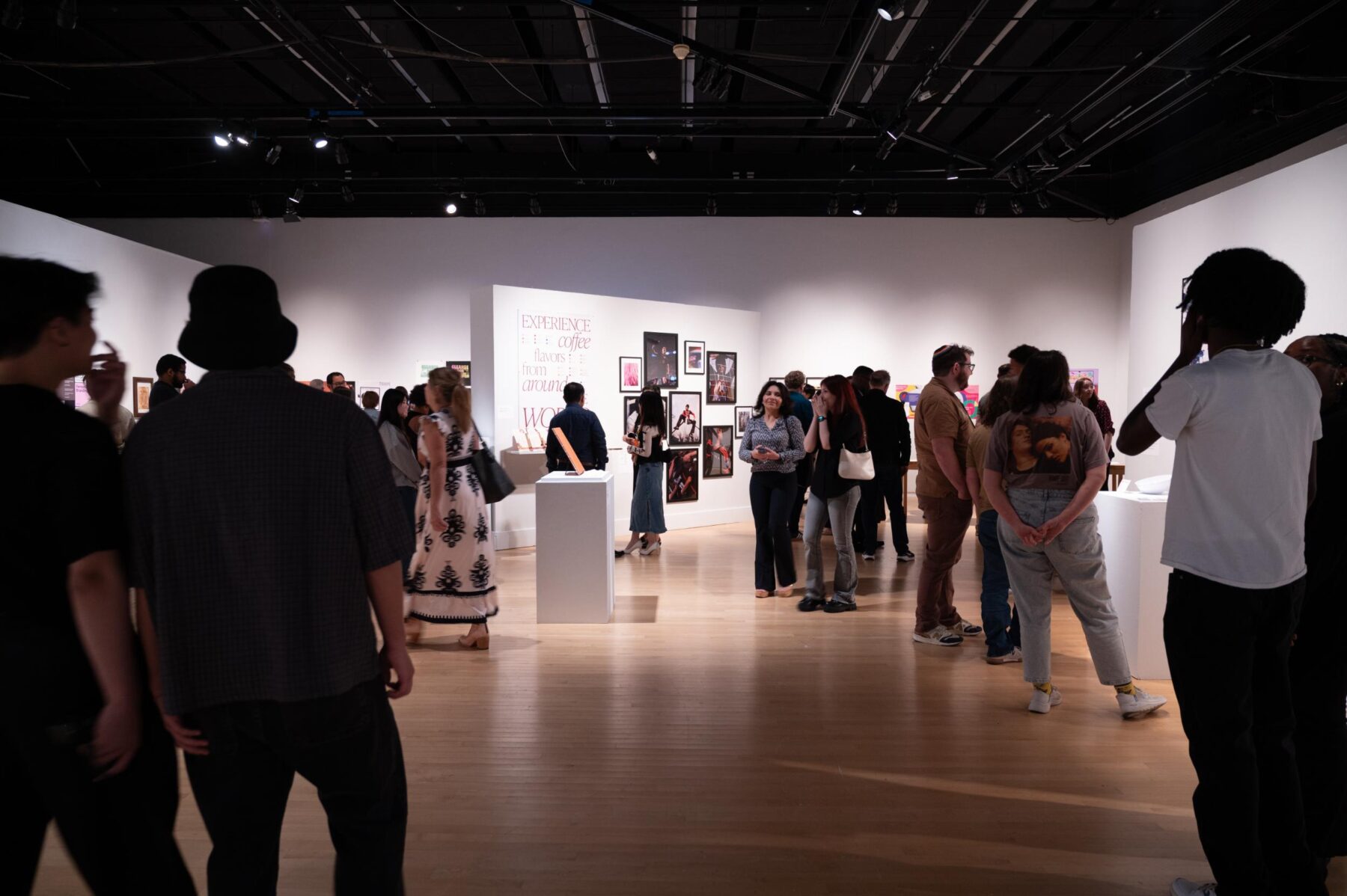 Several visitors gather in a crowded white-walled gallery space.