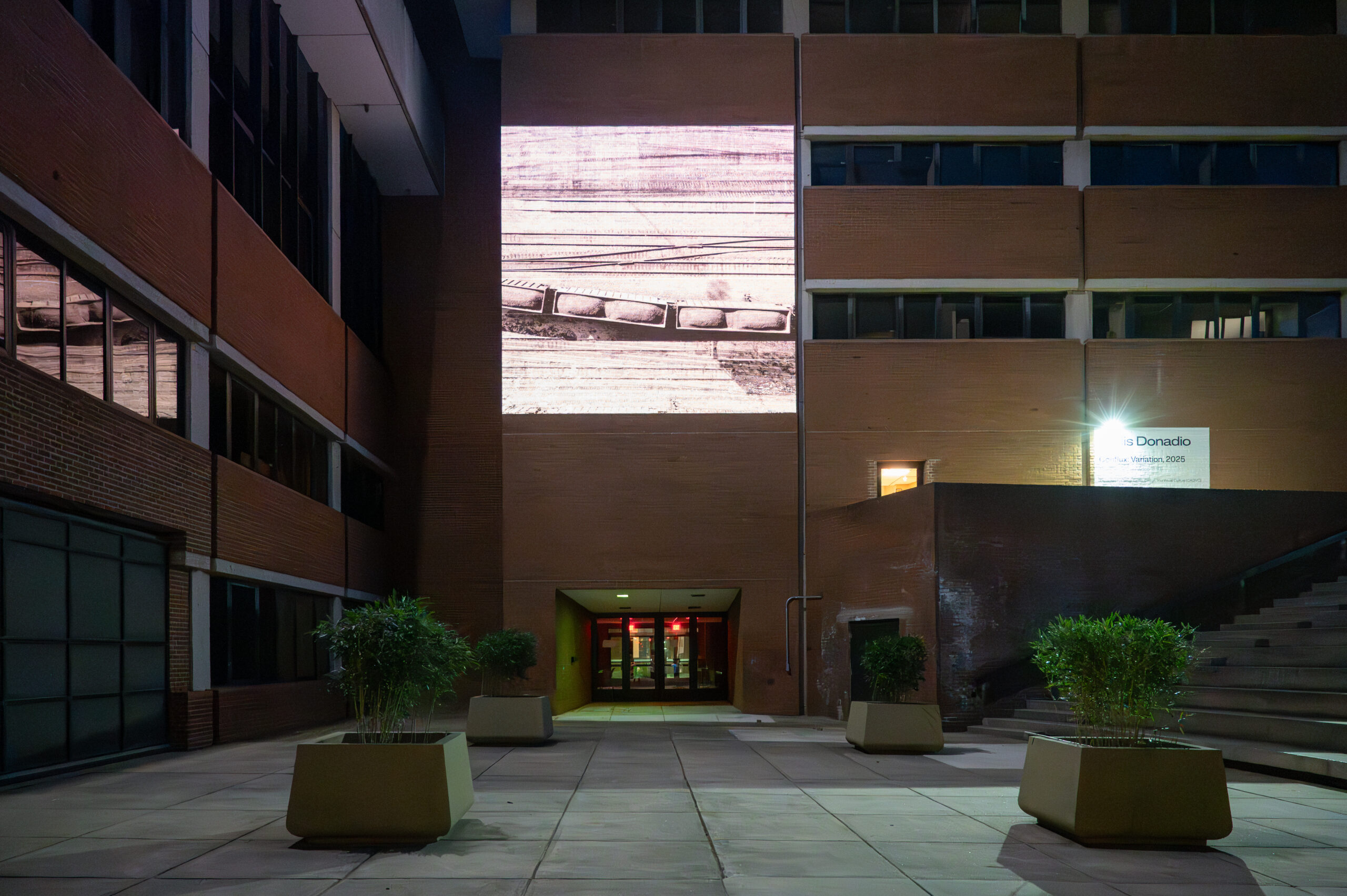 Exterior view of a video projection on a red brick building. Projection shows a monochome birds-eye view of train depot.
