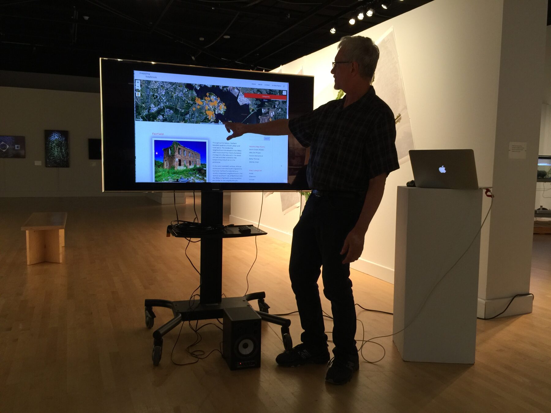 A man in silhouette stands in front of a monitor screen. He is using his right hand to point at something featured on the screen.