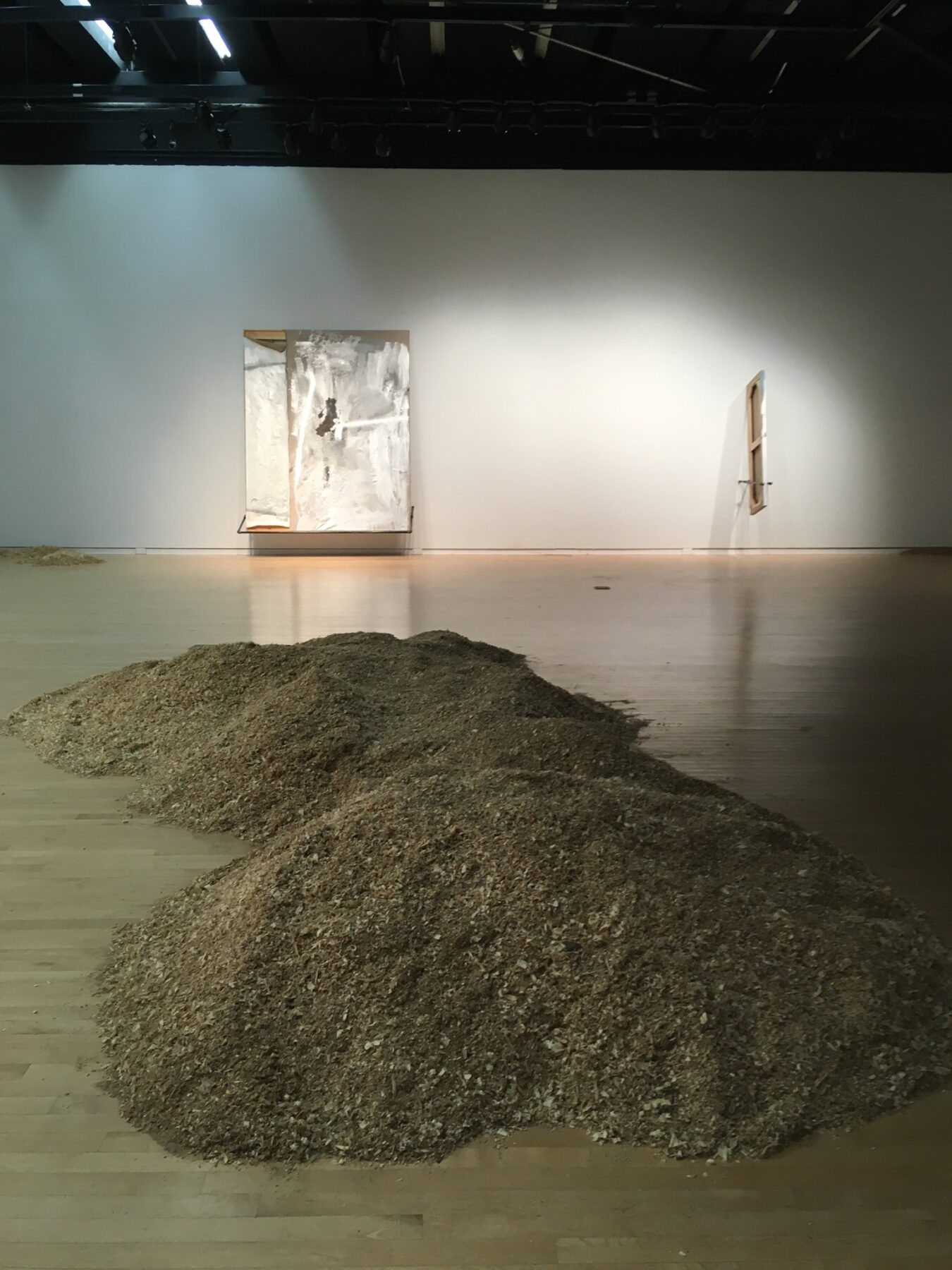 Installation view of a sculpture on the concrete floor of the gallery. Its form resembles a sand dune made out of metallic material.