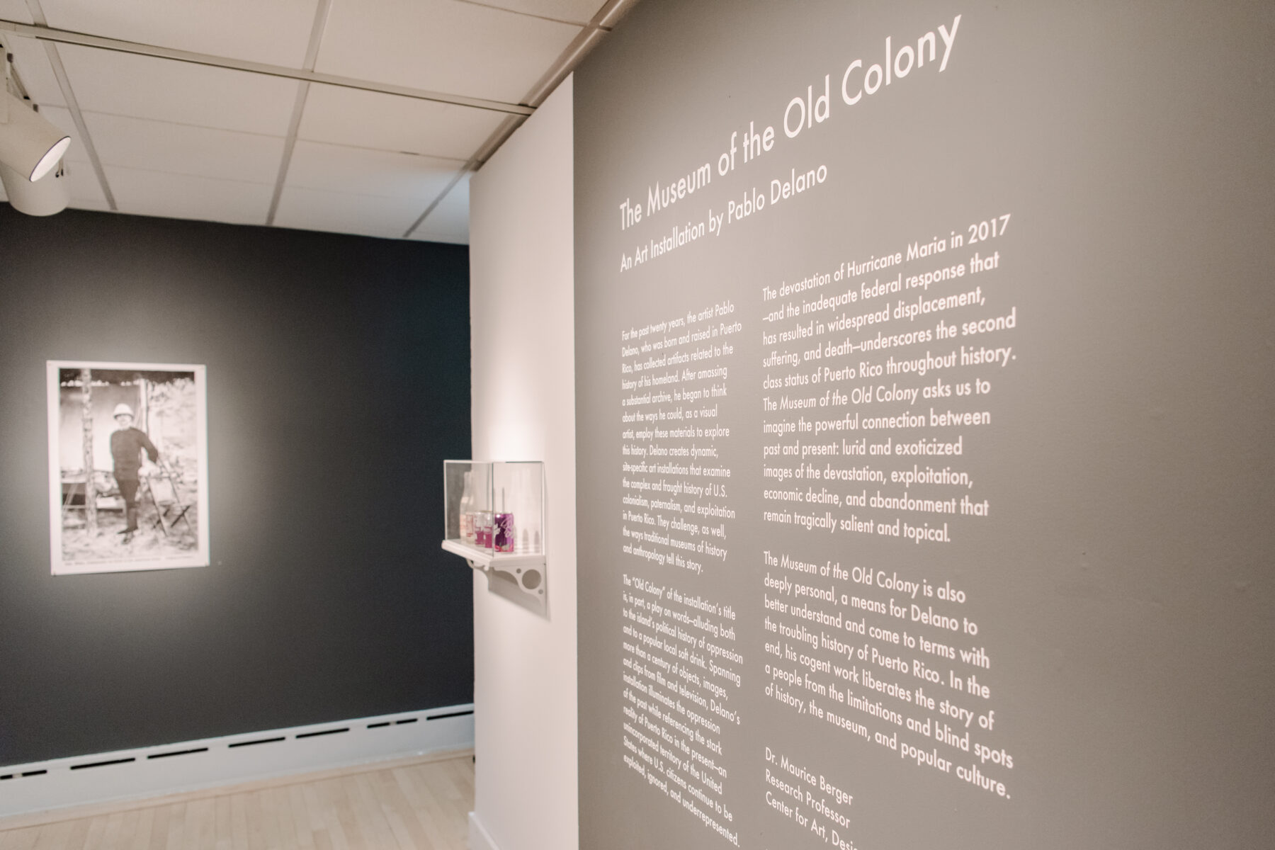Detail photograph of white didactic wall text on a grey gallery wall.