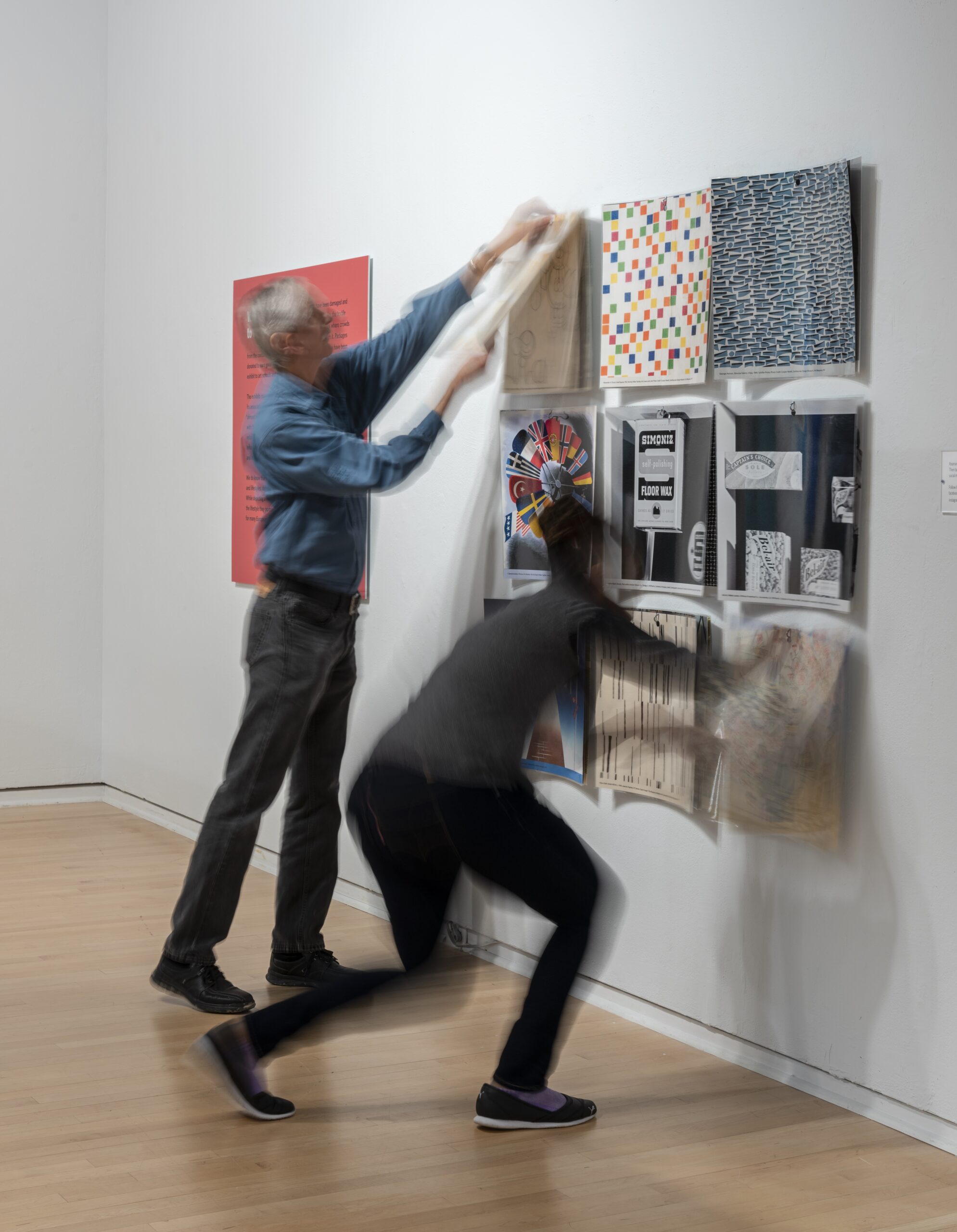 Image of two people whose hands are in quick motion against a wall of nine square panels. Each panel has a unique geometric design.