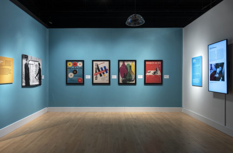A cerulean blue walled gallery with several colorful framed art poster hanging on the walls.
