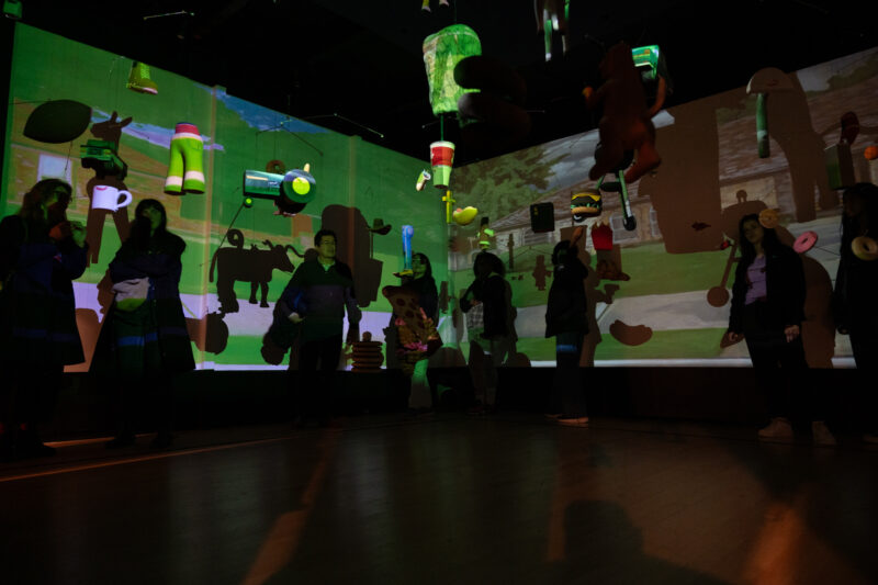 Visitors within an installation in the IMDA MFA Thesis Exhibition. The green-colored work is projected on the walls and the people within.