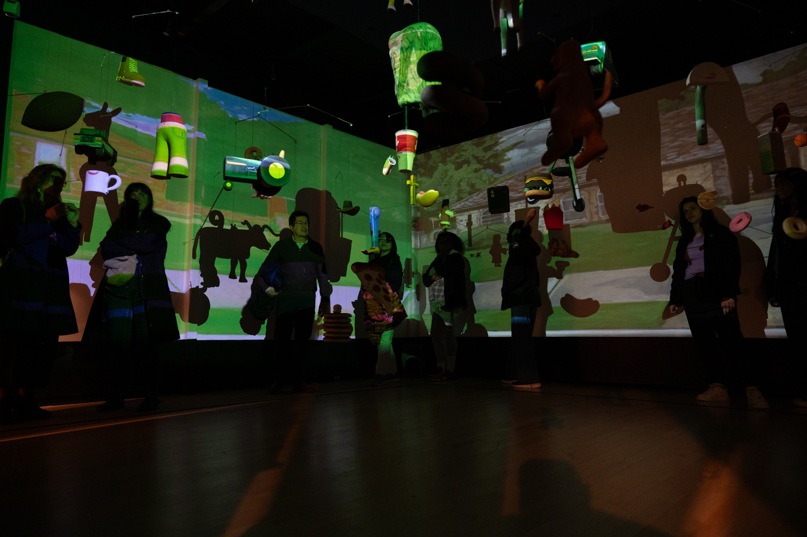 Visitors within an installation in the IMDA MFA Thesis Exhibition. The green-colored work is projected on the walls and the people within.