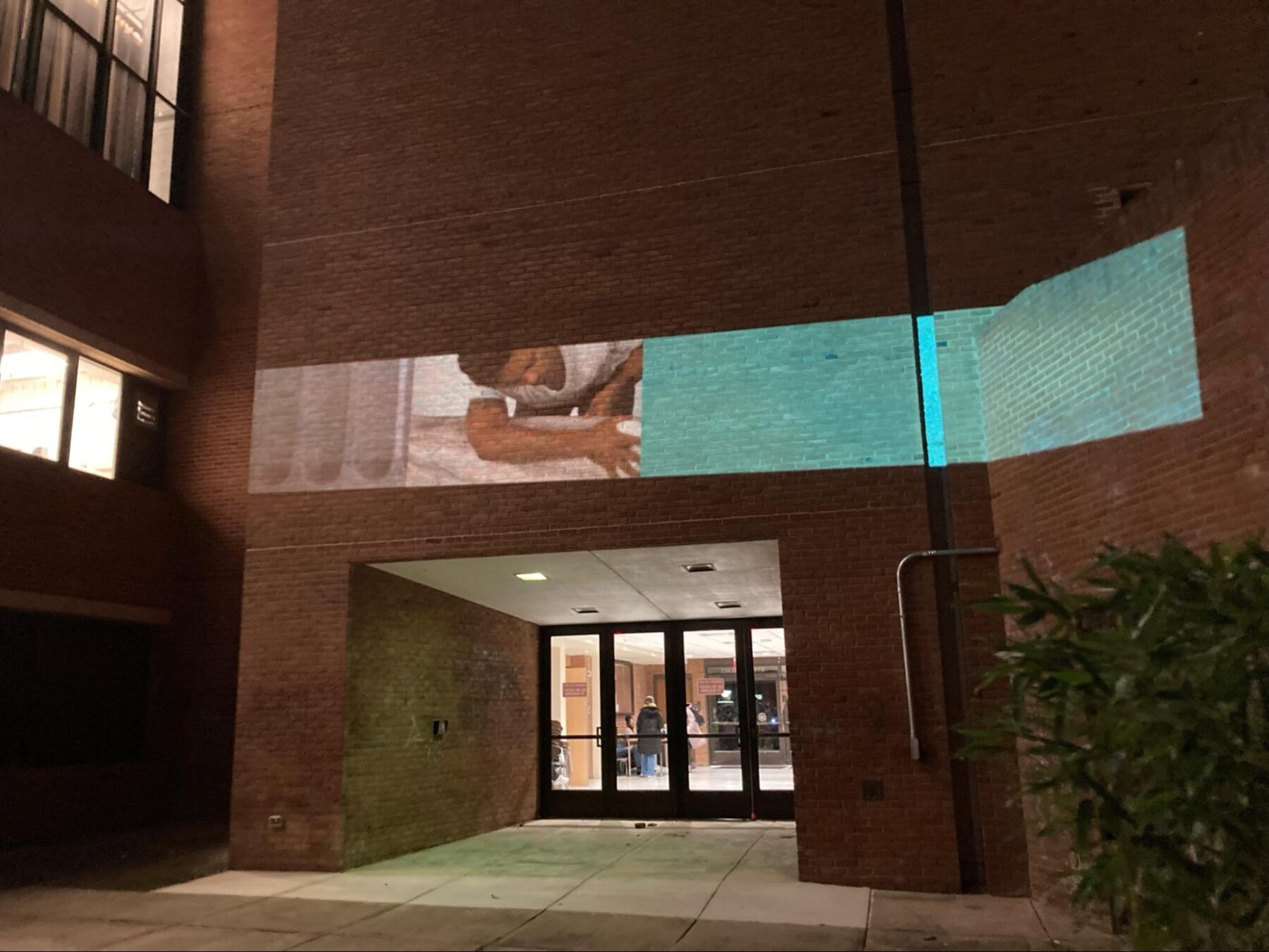A horizontal, narrow video is projected upon the side of a building in the evening.