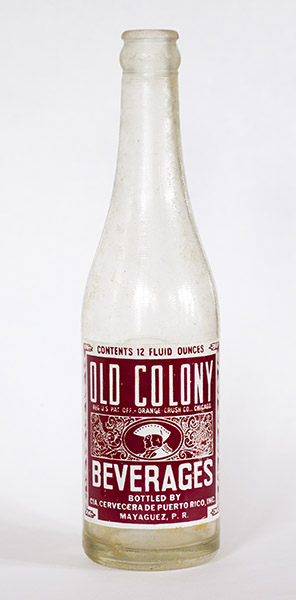 An empty glass bottle with a maroon-and-white label for Old Colony Beverages.