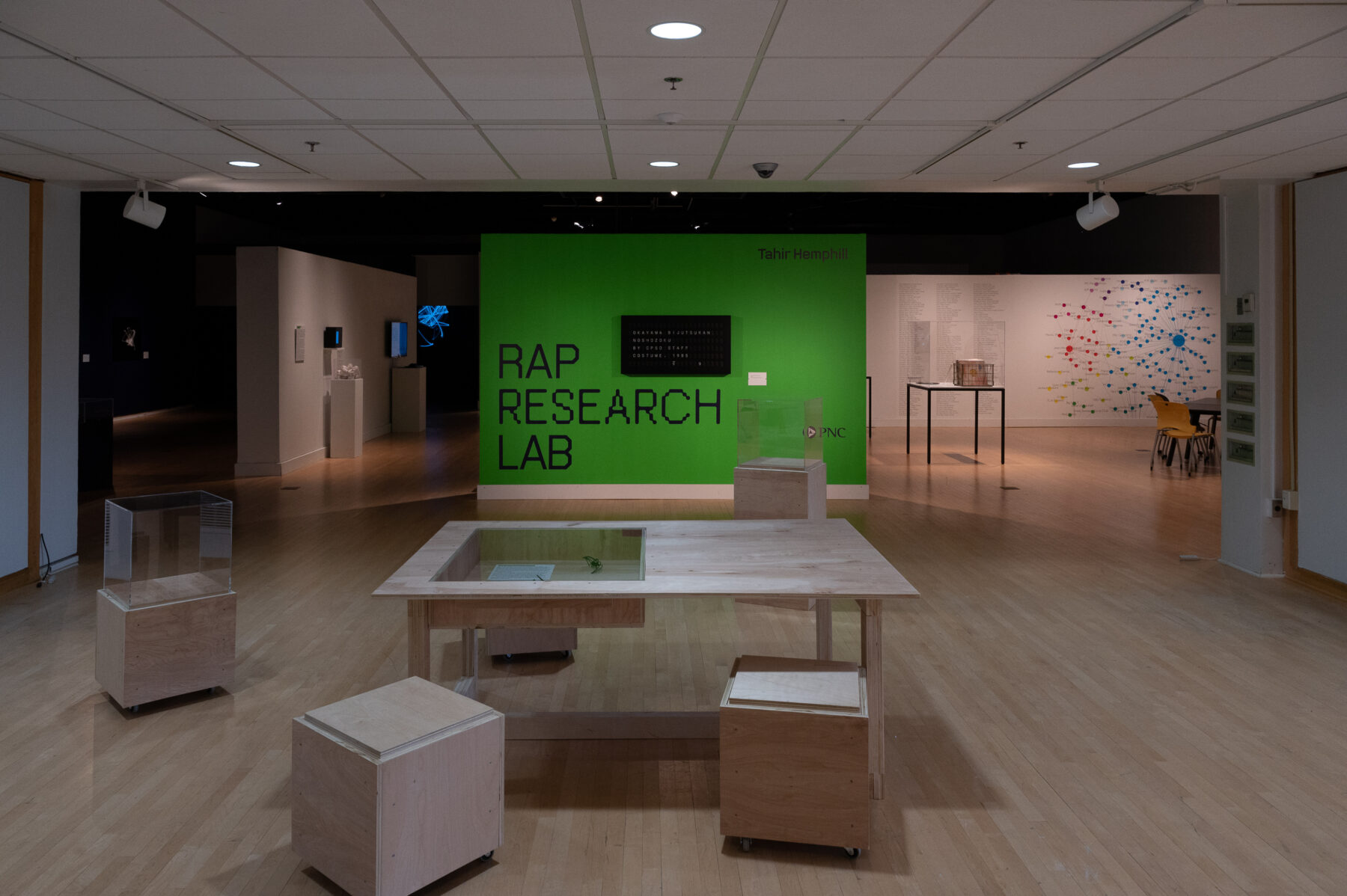 Installation view of Tahir Temphill: Rap Research Lab. A large table with matching components on wheels occupy the center of a gallery. In the background is a bright green wall that reads "Tahir Temphill" and "RAP RESEARCH LAB."
