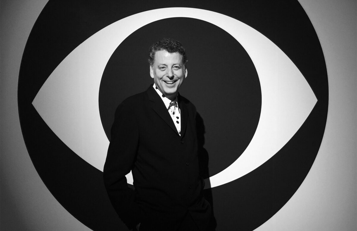 Black and white photograph of Maurice Berger, Chief Curator and research professor at UMBC’s Center for Art, Design and Visual Culture, standing in front of a wall with a large eye-shaped graphic in the background