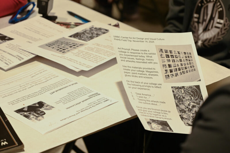 A person out-of-frame holds up a worksheet to read. Other worksheets are piled before them on a white table.