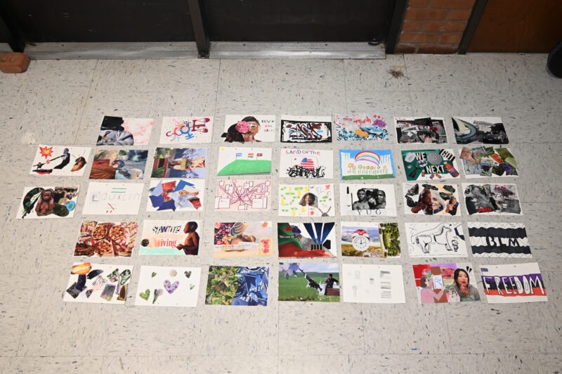 30 works of art are laid on a white linoleum floor. The works are arranged in a 4 x 7 grid with two works to the left. The works consist of collages and drawings.