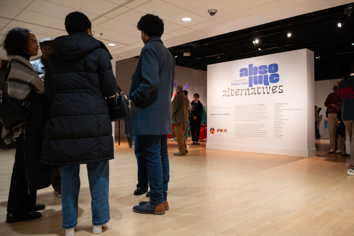 People stand around the front of the gallery as the vinyl wall is highlighted reading "absolute alternatives" with additional show information