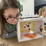 An image of an OCA Mocha Kids Club artist showing off their Button Museum from the "Make Your Own Museum" craft.